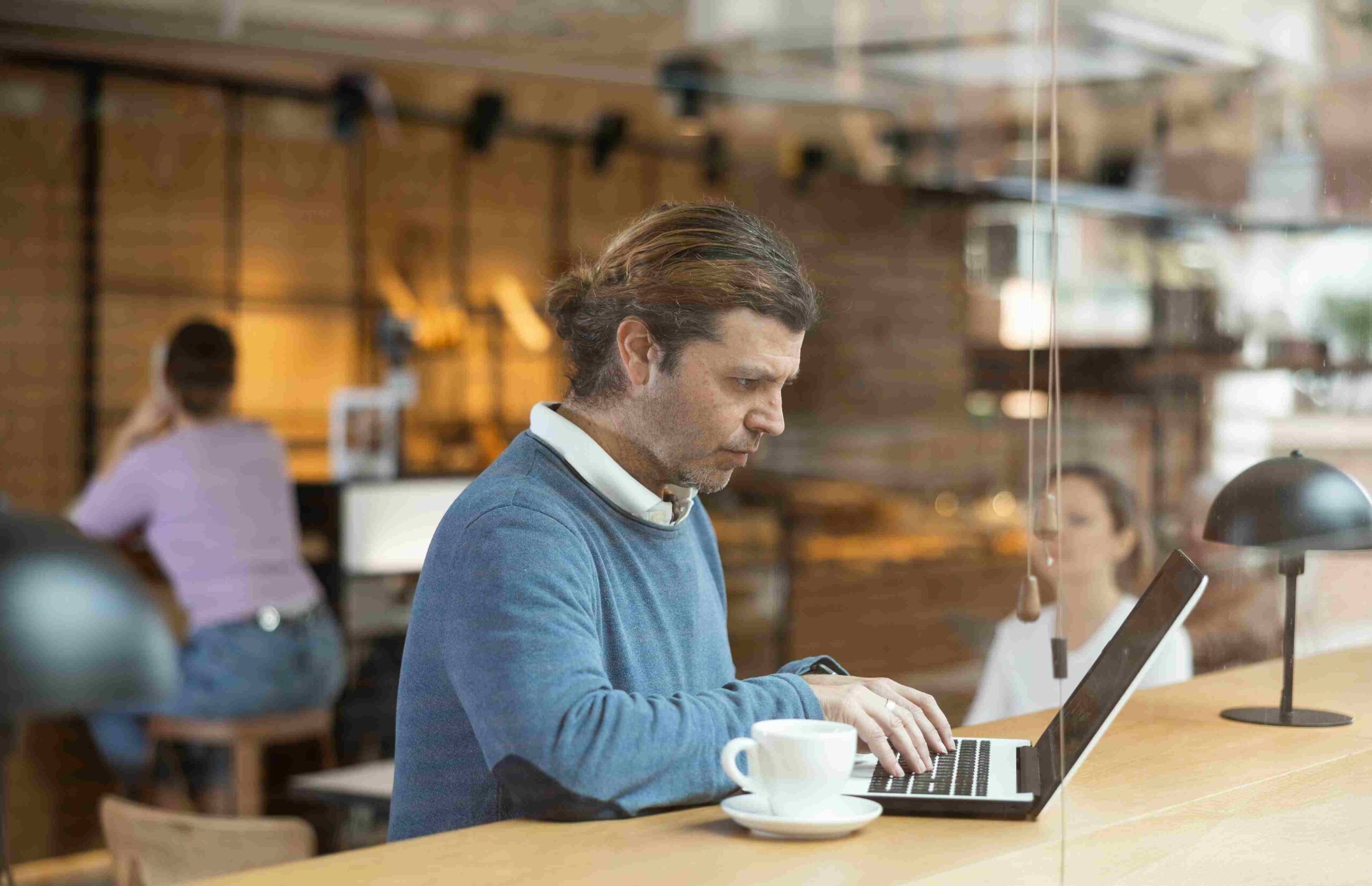 Muškarac radi na laptopu u modernom kafiću sa šoljicom kafe na stolu
